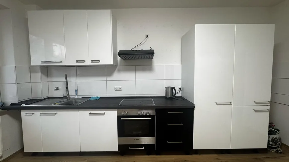 Frontansicht einer weißen Küchenzeile mit Backofen, dunklem Schubladenschrank und Hochschränken